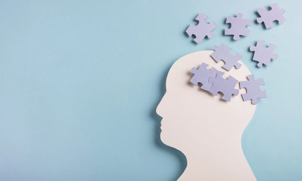 Imagem ilustrativa de uma cabeça humana em formato de quebra-cabeça, com peças flutuando, simbolizando o processo criativo e o raciocínio. Ideal para conteúdos sobre mente e inteligência e saúde mental, que tem relação com a atualização da NR 1