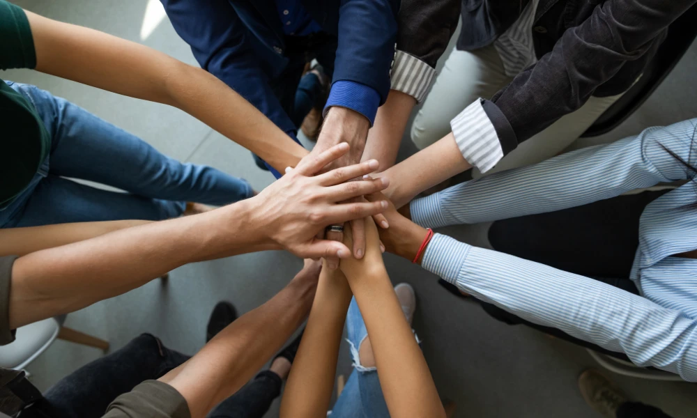 Diversas mãos se unindo em um gesto de união e colaboração, refletindo o trabalho em equipe e a importância da colaboração entre as pessoas.