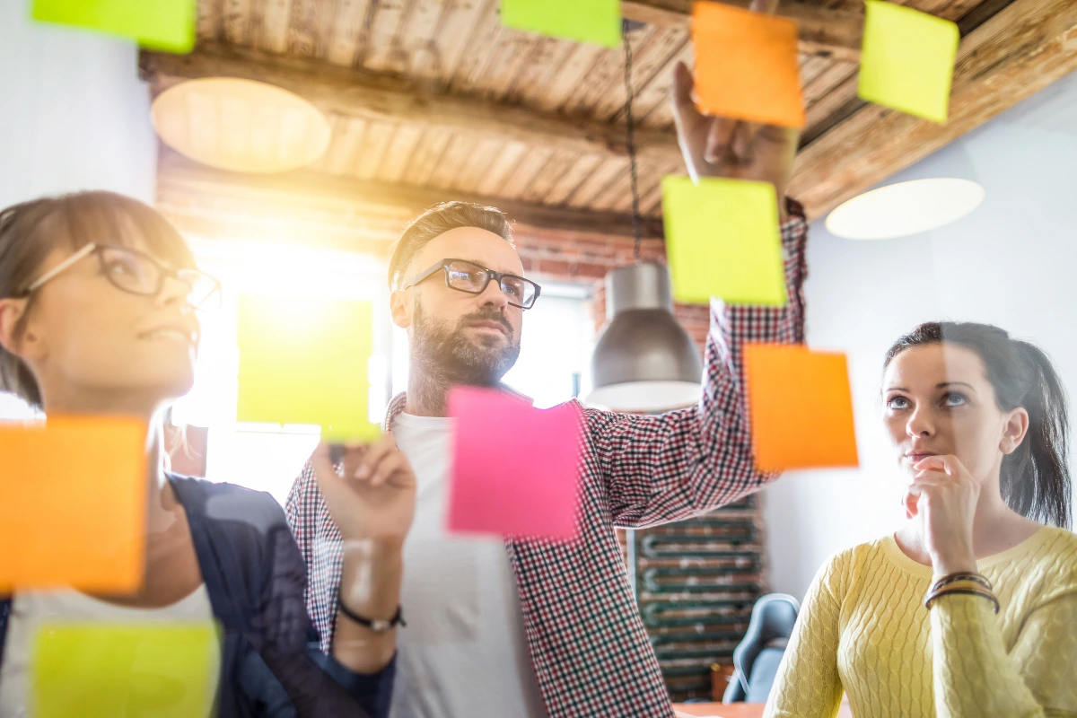 Equipe de profissionais em uma reunião criativa com quadros de post-its coloridos na parede, discutindo ideias inovadoras no ambiente de escritório moderno.