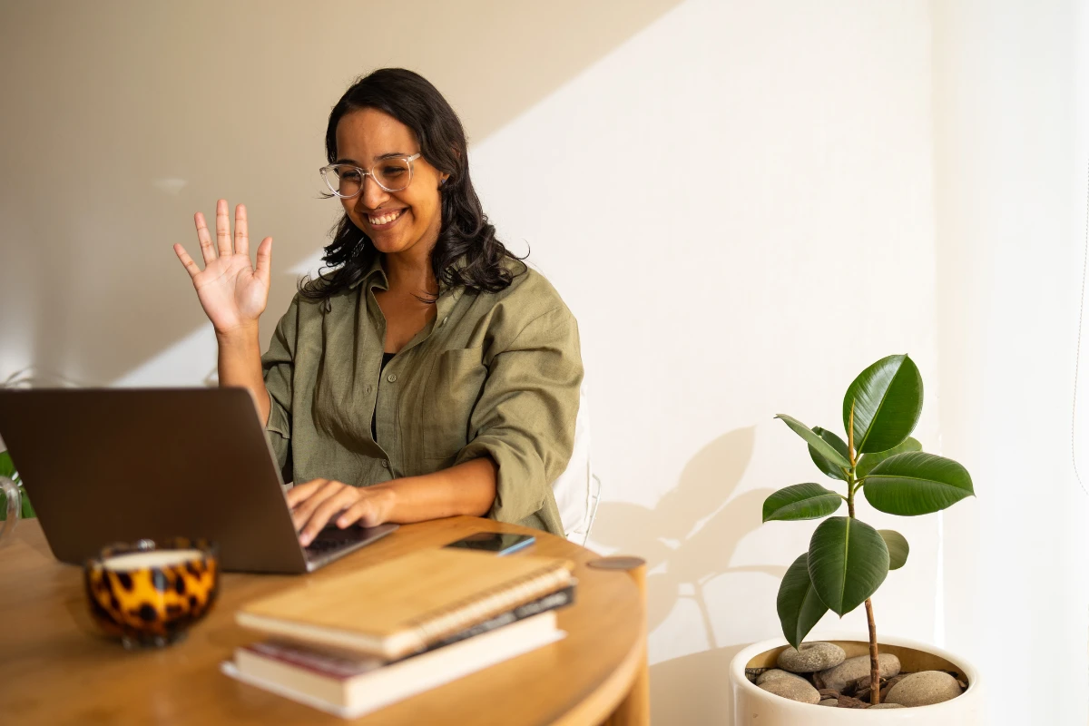 Mulher sorridente usando laptop em um ambiente de trabalho com uma planta ao lado, simbolizando produtividade e bem-estar. Ela faz parte do programa de buddt system na empresa.