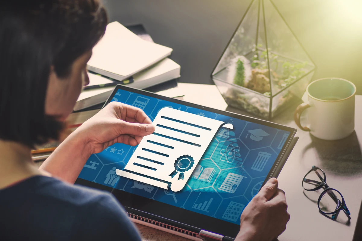 Pessoa segurando um certificado digital sobre um tablet em ambiente de trabalho, com itens de escritório ao fundo, simbolizando conquistas profissionais.