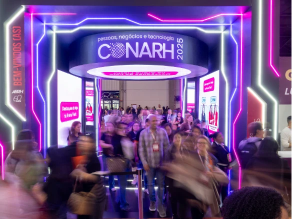 Entrada de evento de tecnologia e negócios com faixa neon e pessoas circulando em área iluminada, com destaque para o painel “C6 NARH 2025” no estande.